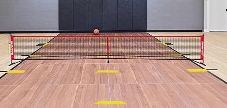 Red and black Bearwill pickleball net on an indoor court with a basketball at the back.