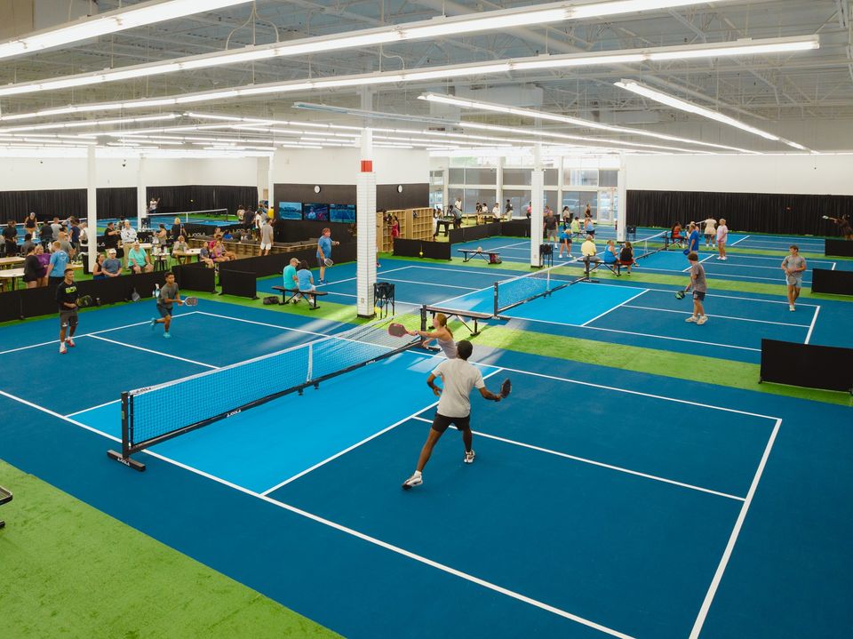 A doubles match on the go inside Pickleball 901 facilities. 3 other blue courts are pictured in the background.