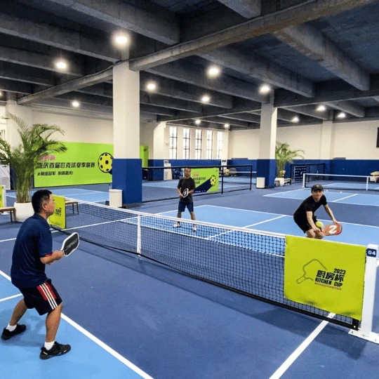 A match of pickleball doubles in China on an indoor blue court.